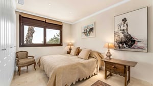 Comfortable bedroom with a neutral palette, featuring a double bed, classic armchair, wooden nightstands, and artwork on the walls.