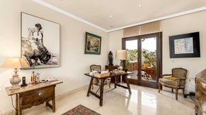 Cozy home office or guest room with traditional wooden furniture, armchairs, and glass doors opening onto a green and peaceful terrace.
