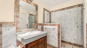 Classic bathroom with a walk-in shower, marble-tiled walls in warm tones, and a single vanity unit. The large mirror and natural light enhance the space’s warmth and functionality.