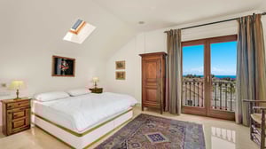 Spacious master bedroom featuring a king-sized bed, skylight, traditional wooden furniture, and glass doors opening onto a terrace with panoramic sea views.