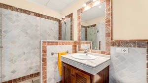Refined bathroom decorated with warm-toned marble tiles, featuring a walk-in shower, vanity with under-sink storage, and a wide mirror.