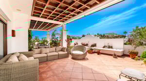 Expansive terrace with terracotta tiles, comfortable wicker furniture, a circular lounge chair, potted plants, and a white bench with decorative fountain detail.