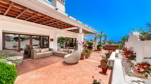 Wide terrace featuring shaded outdoor seating, lush greenery, and a white built-in fountain wall adorned with vibrant potted flowers.