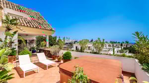Sunny rooftop terrace with a hot tub, two white sun loungers, and abundant tropical plants offering partial sea views and privacy.