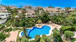 Overhead view of an organically shaped pool surrounded by lush tropical gardens and elegant apartment buildings with classic tiled roofs.