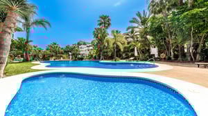 Close-up view of a resort-style swimming pool set amid manicured gardens, palm trees, and sun loungers, evoking a luxurious tropical escape.
