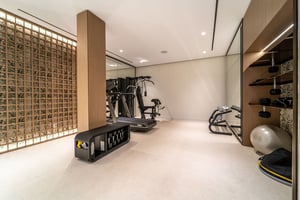 Modern home gym with minimalist design, featuring a treadmill, weight station, dumbbells, and a decorative wood panel wall with soft lighting.