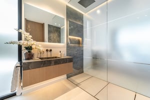 Modern bathroom with a floating marble vanity, large mirror, frosted glass shower enclosure, and elegant lighting.