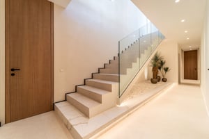 Elegant hallway with a floating staircase featuring a glass balustrade, recessed lighting, and indoor plants in a stone bed.
