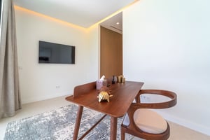 Minimalist home office with a wooden desk and designer chair, flat-screen TV on the wall, and indirect ceiling lighting.