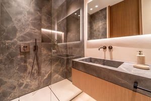 Modern bathroom with dark marble walls, glass walk-in shower, floating vanity with integrated sink, and backlit mirror.