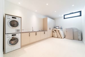 Spacious laundry room with stacked washer and dryer, light cabinetry, ample storage space, and a small high-set window.