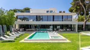 Luxury modern villa in Marbella with private pool, sun loungers, outdoor lounge areas, and floor-to-ceiling glass windows surrounded by landscaped garden.