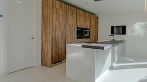 Contemporary kitchen featuring a central white island with black sink, built-in wooden cabinetry, and a wall-mounted TV.