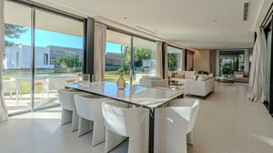 Bright dining area with a glossy rectangular table, upholstered beige chairs, and views of the open-plan living room and garden.