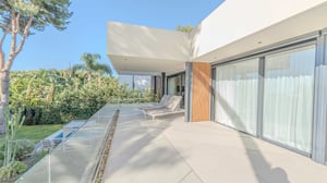 Expansive upper terrace with sun loungers, glass railing, and views of a tropical garden with palm trees and manicured greenery.