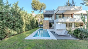 View of the swimming pool lined with privacy hedges, lounge chairs, and the rear facade of the modern villa surrounded by greenery.
