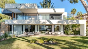 Front view of a modern two-story villa with minimalist architecture, featuring floor-to-ceiling glass windows, outdoor lounge and dining areas, and surrounded by lush greenery and palm trees.