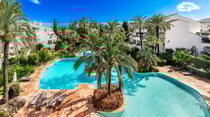 Resort-style pool area with crystal-clear water, tropical landscaping, sun loungers, and Mediterranean architecture in an exclusive residential complex.